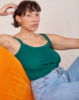 Tiara is sitting on a orange upholstered chair wearing Cropped Cami in Hunter Green and light wash Sailor Jeans