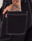 Carpenter Jeans in Black back pocket close up. Jesse has their hand in the pocket.