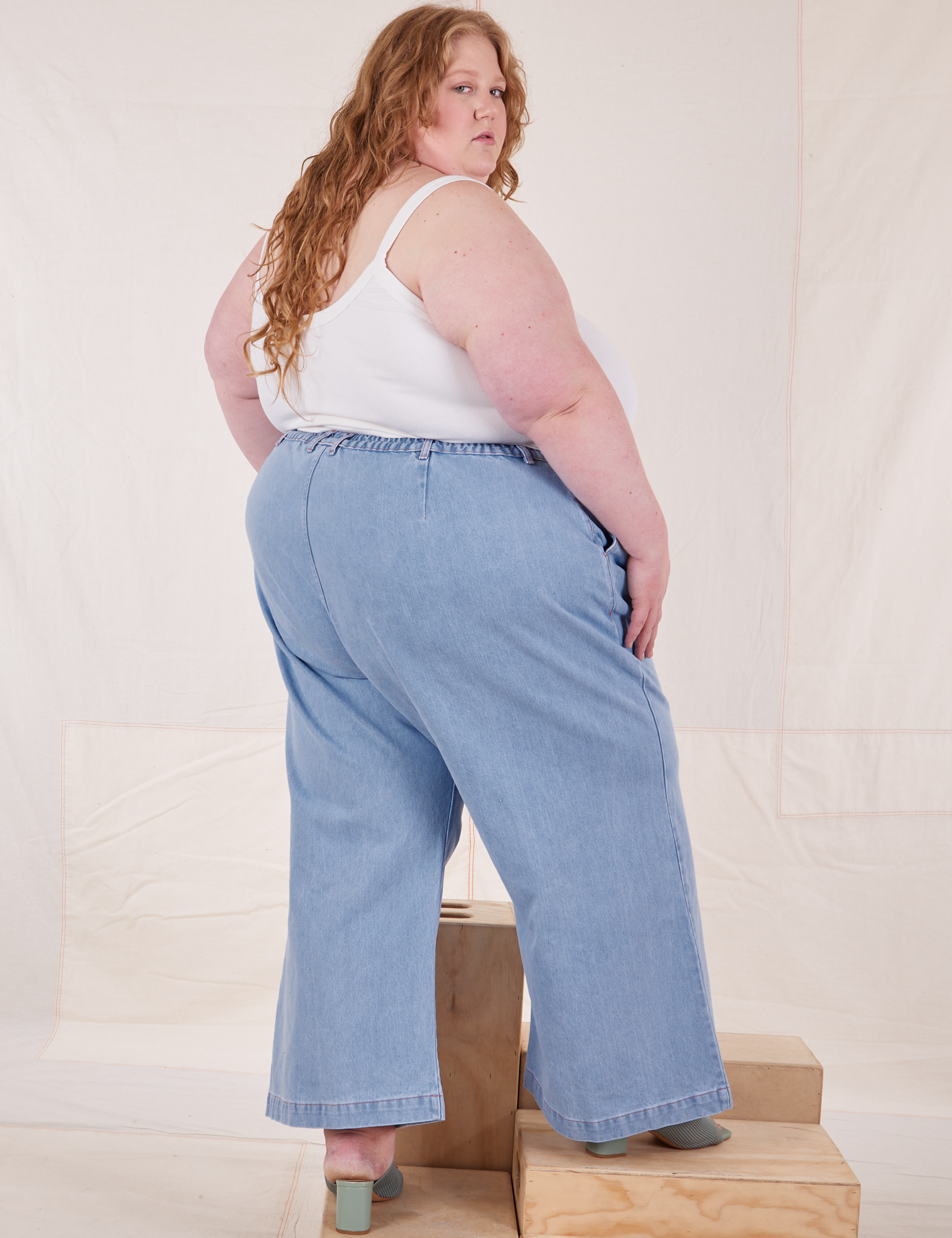 Angled back view of Indigo Wide Leg Trousers in Light Wash and vintage off-white Cami on Catie