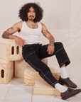 Jesse is sitting on a wooden crate. They are wearing Carpenter Jeans in Black and Tank Top in vintage tee off-white