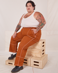 Sam is wearing Carpenter Jeans in Burnt Terracotta and Tank Top in vintage tee off-white. They are sitting on a stack of wooden crates.