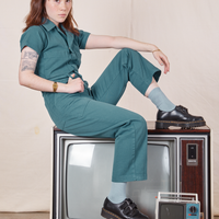 Hana is sitting sideways on a vintage tv wearing Petite Short Sleeve Jumpsuit in Marine Blue
