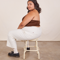 Alicia is sitting on a vintage stool facing the left side. She is wearing Halter Top in Fudgesicle Brown and vintage off-white Western Pants.