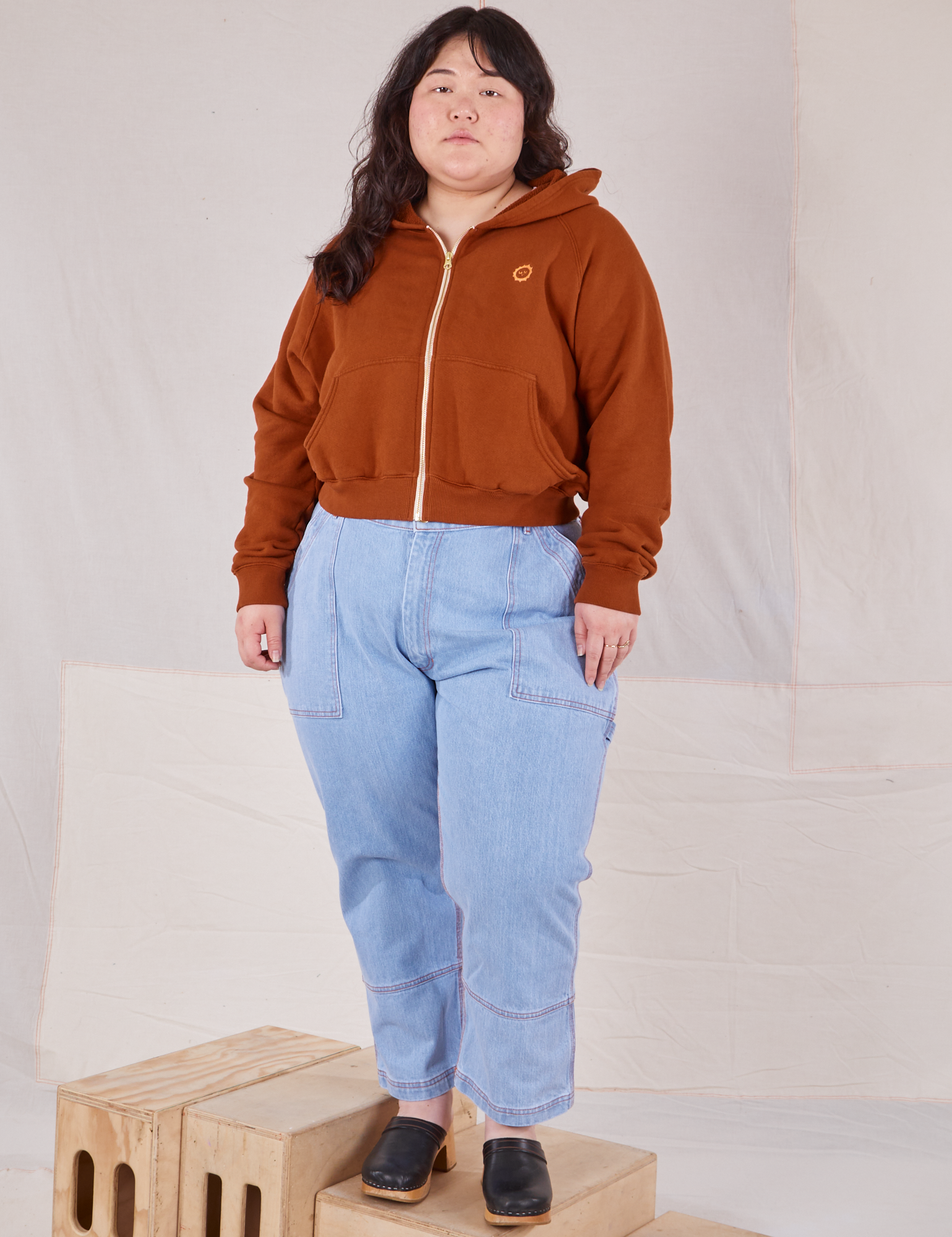 Ashley is wearing Cropped Zip Hoodie in Burnt Terracotta and light wash Carpenter Jeans