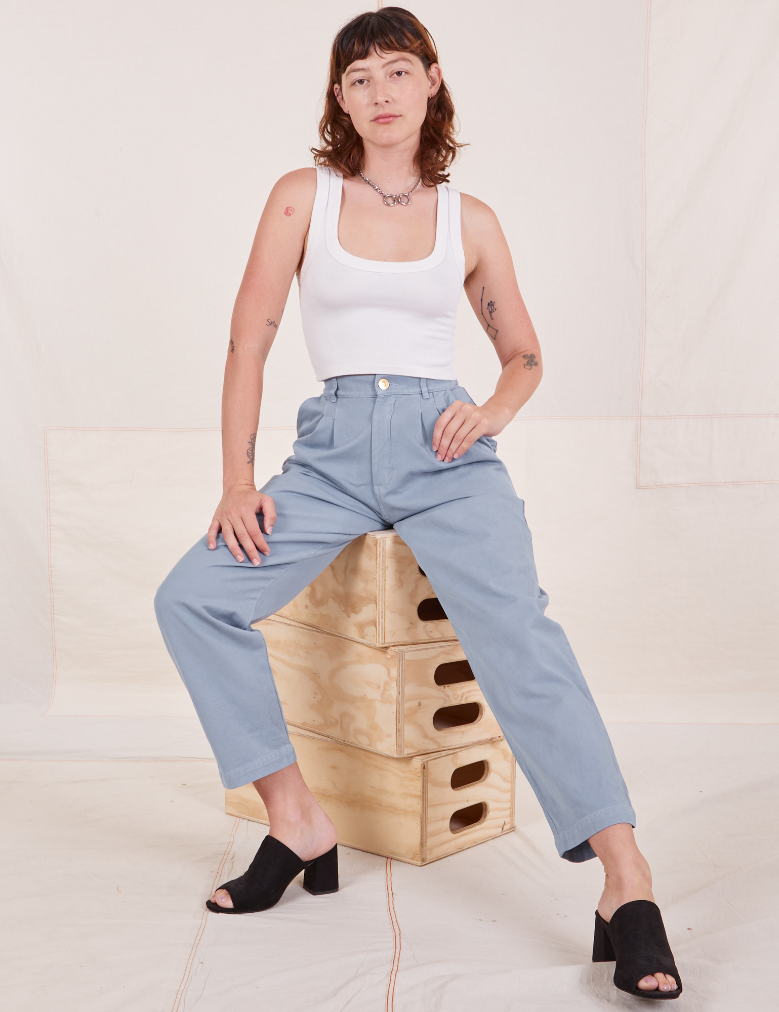 Alex is sitting on a stack of wooden crates wearing Organic Trousers in Periwinkle and Cropped Tank Top in vintage tee off-white
