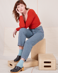 Alex is sitting on a wooden crate wearing Railroad Stripe Denim Work Pants and paprika Wrap Top