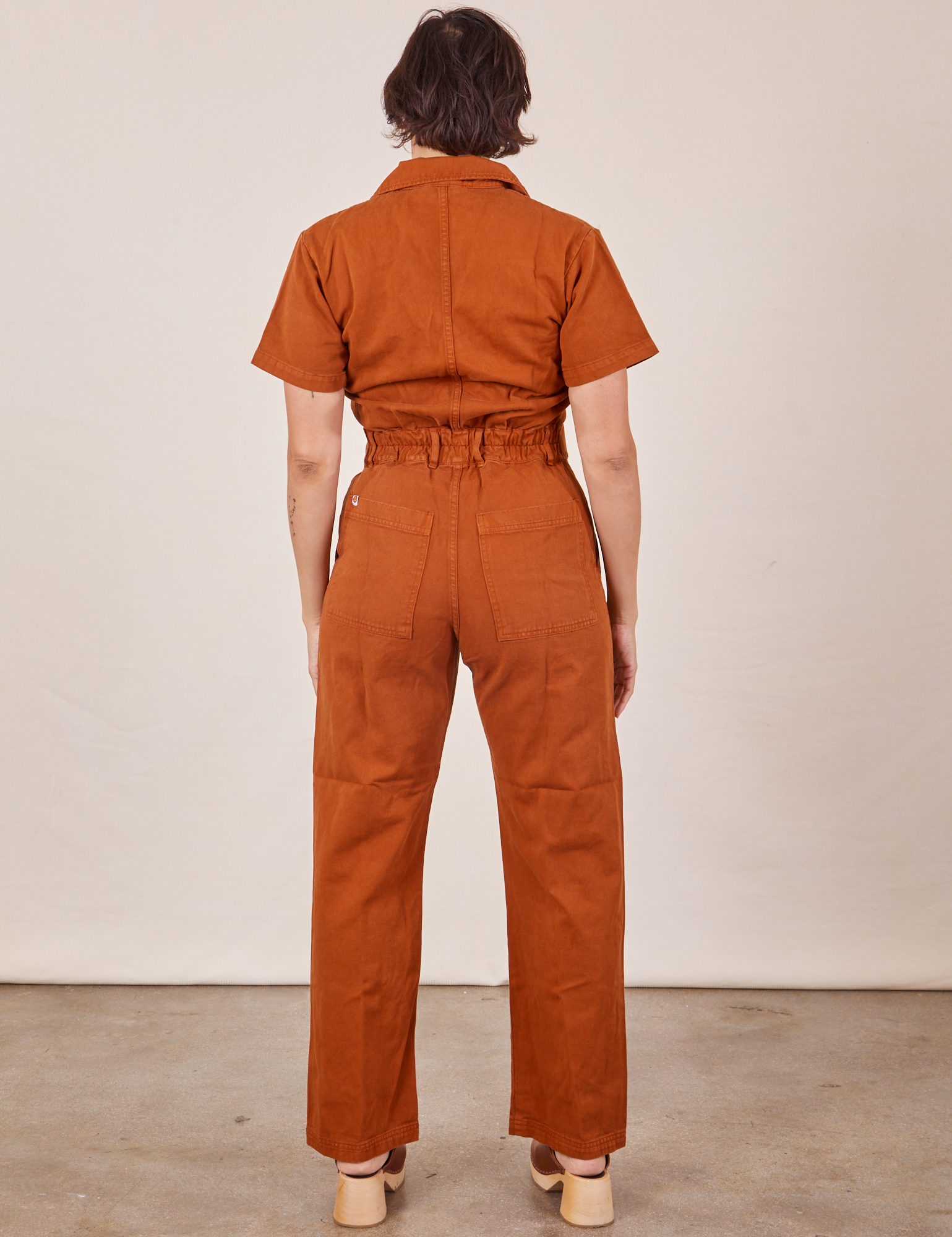 Back view of Short Sleeve Jumpsuit in Burnt Terracotta worn by Tiara