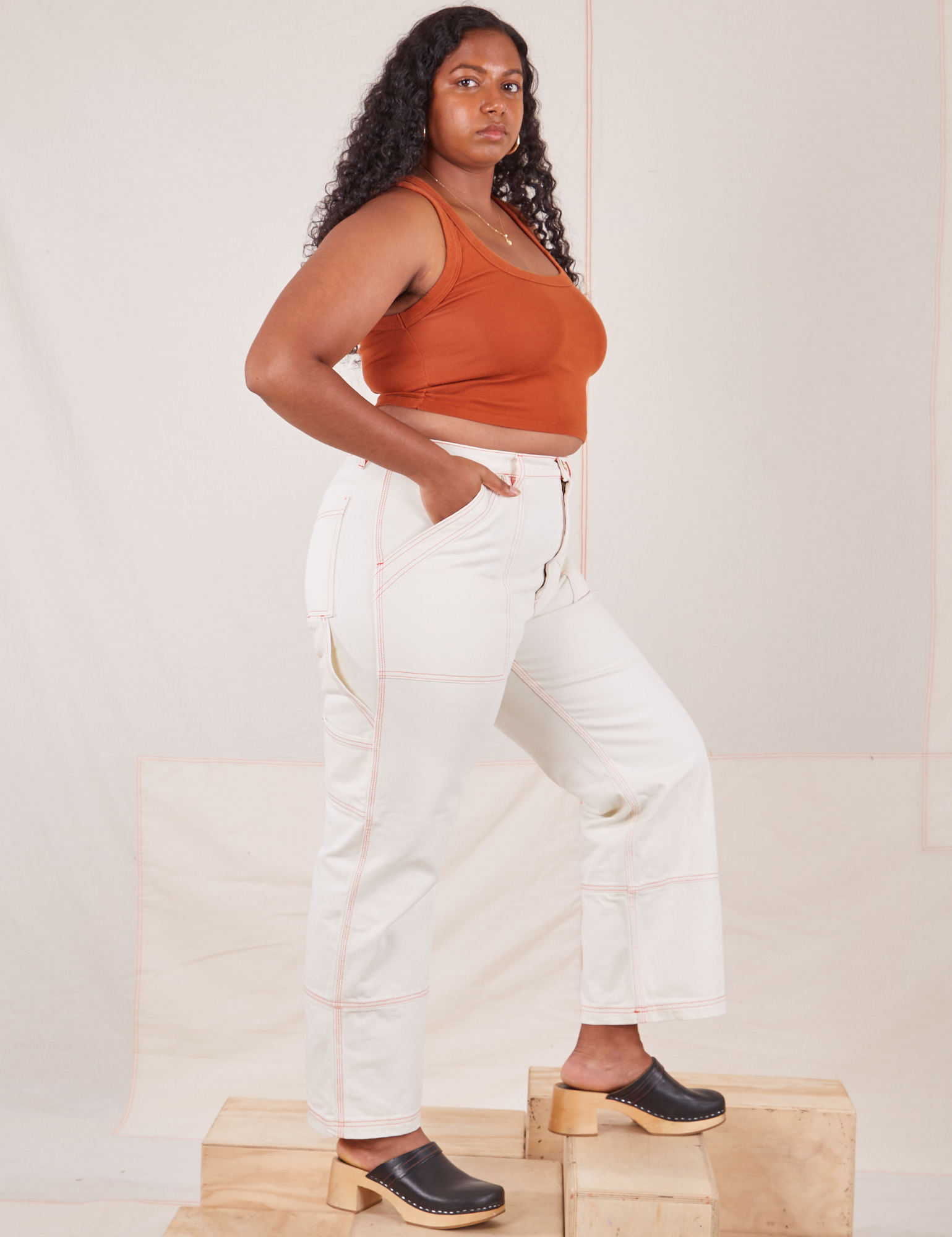 Side view of Carpenter Jeans in Vintage Tee Off-White and burnt terracotta Cropped Tank Top on Meghna