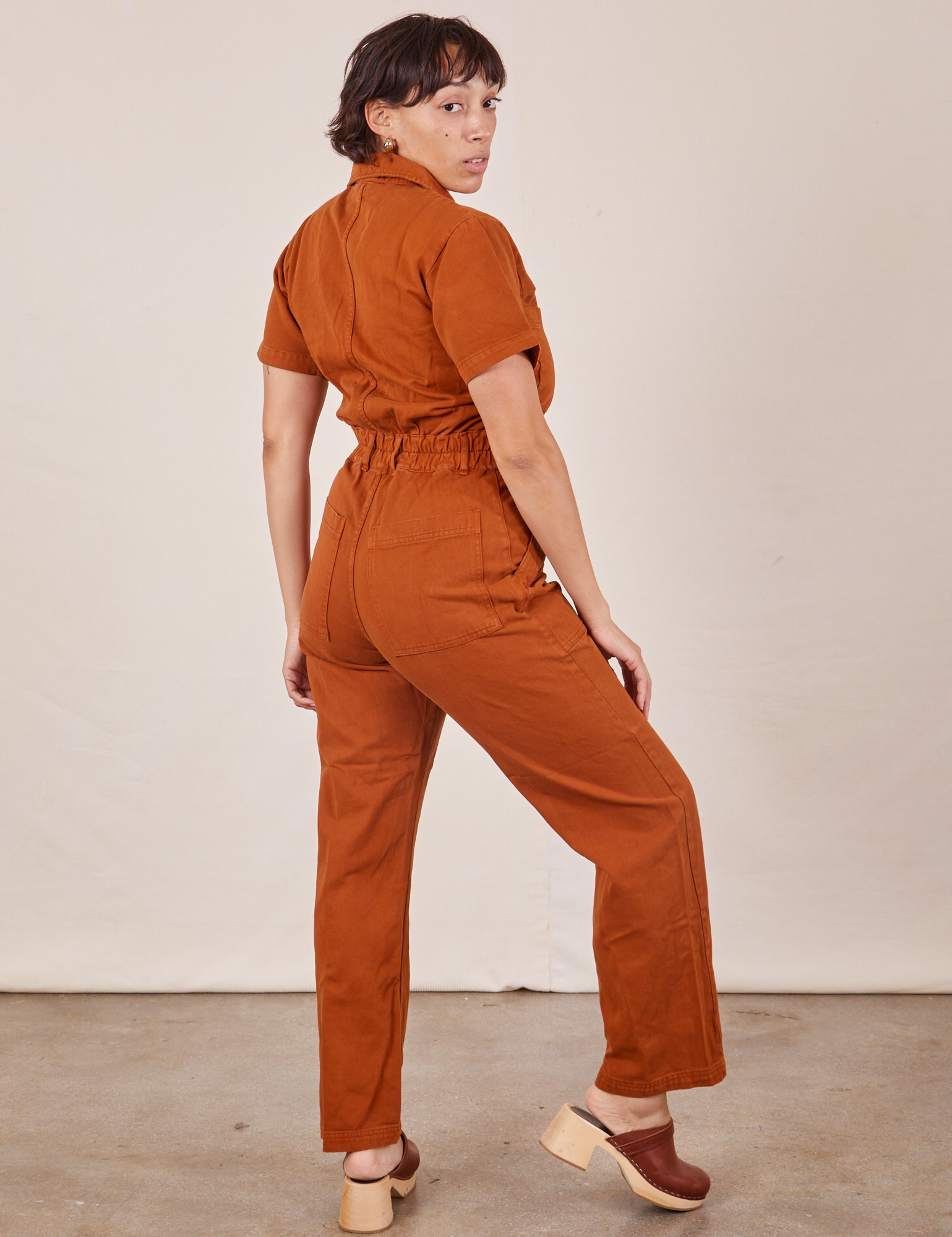Angled back view of Short Sleeve Jumpsuit in Burnt Terracotta worn by Tiara