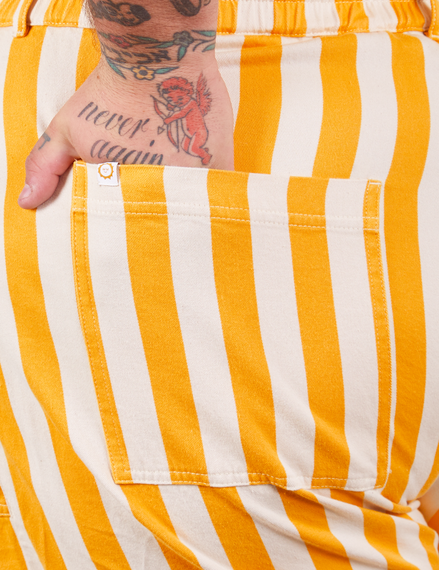 Lemon Stripe Jumpsuit back pocket close up. Sam has their hand in the pocket.