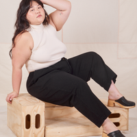 Ashley is wearing Heavyweight Trousers in Basic Black and vintage off-white Sleeveless Turtleneck. She is sitting on a wooden crate.