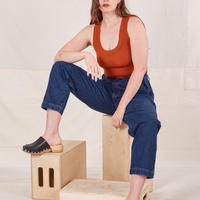 Allison is sitting on a wooden crate wearing Denim Trouser Jeans in Dark Wash and a burnt orange Tank Top