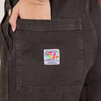 Back pocket close up of Original Overalls in Mono Espresso. Tiara has her hand in the pocket.