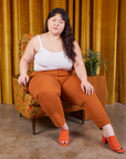 Ashley is sitting on a upholstered chair wearing Petite Pencil Pants in Burnt Terracotta and Cropped Cami in vintage tee off-white