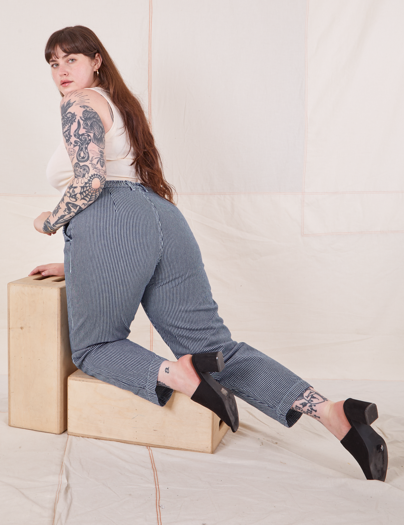 Sydney is kneeling on a wooden crate wearing Denim Trouser Jeans in Railroad Stripe