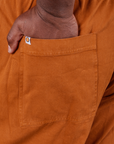 Back pocket close up of Short Sleeve Jumpsuit in Burnt Terracotta. Elijah has his hand in the pocket.