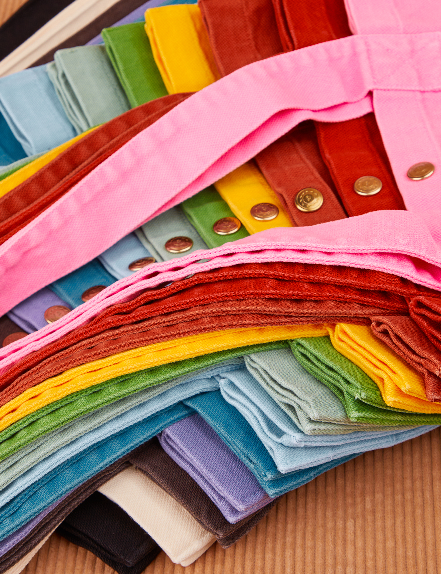 Shopper Tote Bag in a rainbow of hues stacked on top of one another.
