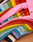 Shopper Tote Bag in a rainbow of hues stacked on top of one another.