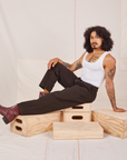 Jesse is sitting on a wooden crate. They are wearing Heavyweight Trousers in Espresso Brown and Cropped Tank Top in vintage tee off-white