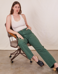 Allison is sitting in a vintage brown office chair wearing Work Pants in Dark Emerald Green and vintage off-white Tank Top