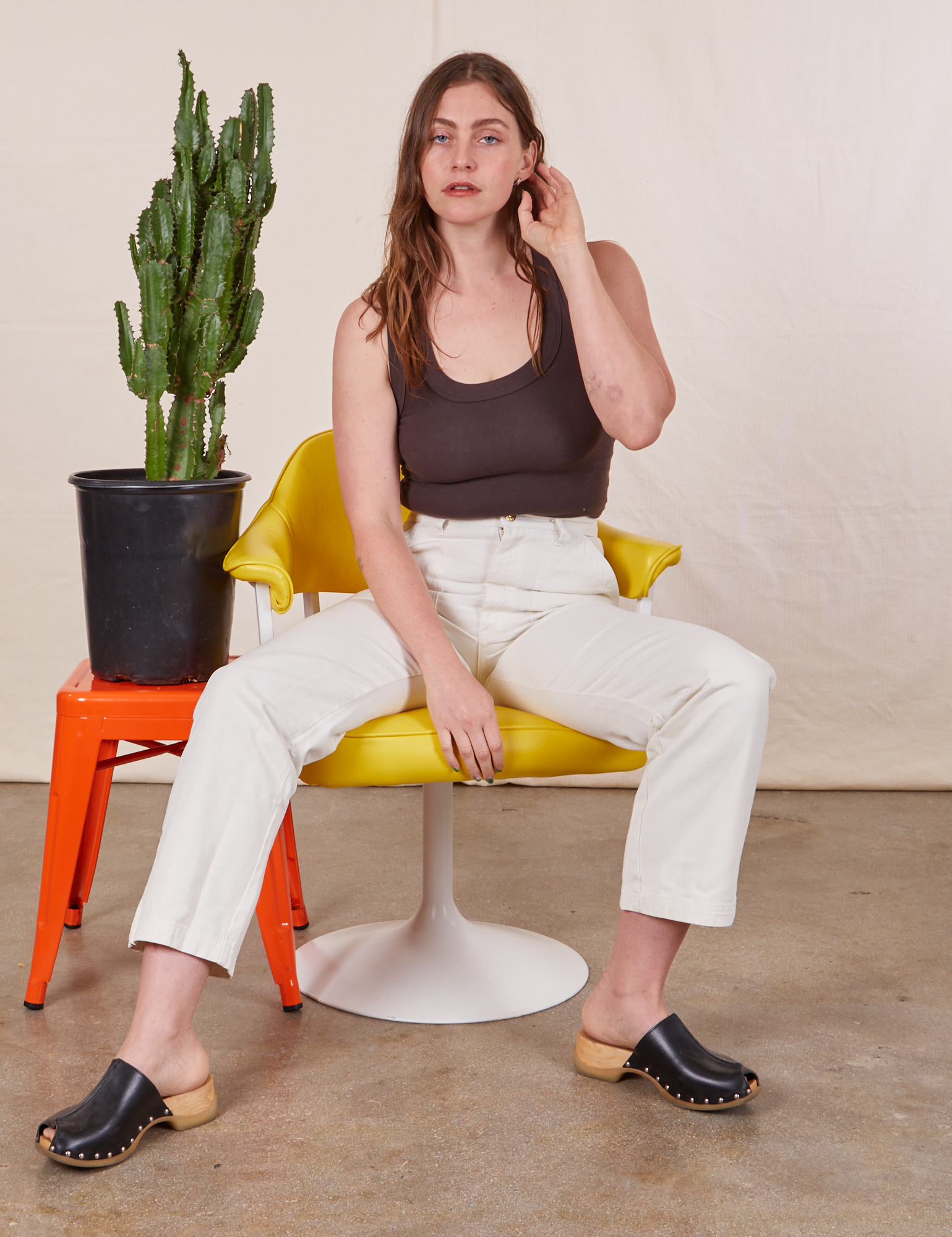 Allison is sitting in a yellow and white chair wearing Work Pants in Vintage Tee Off-White and an espresso brown Tank Top