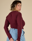 Angled back view of Mika wearing the Red wine Long Sleeve Baby Tee