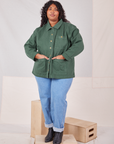 Morgan is wearing a buttoned up Denim Work Jacket in Dar Green Emerald. She has both hands in the front pockets.