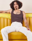 Jesse is wearing Western Pants in Vintage Tee Off-White and espresso brown Tank Top. They are sitting in a vinyl yellow dining booth.