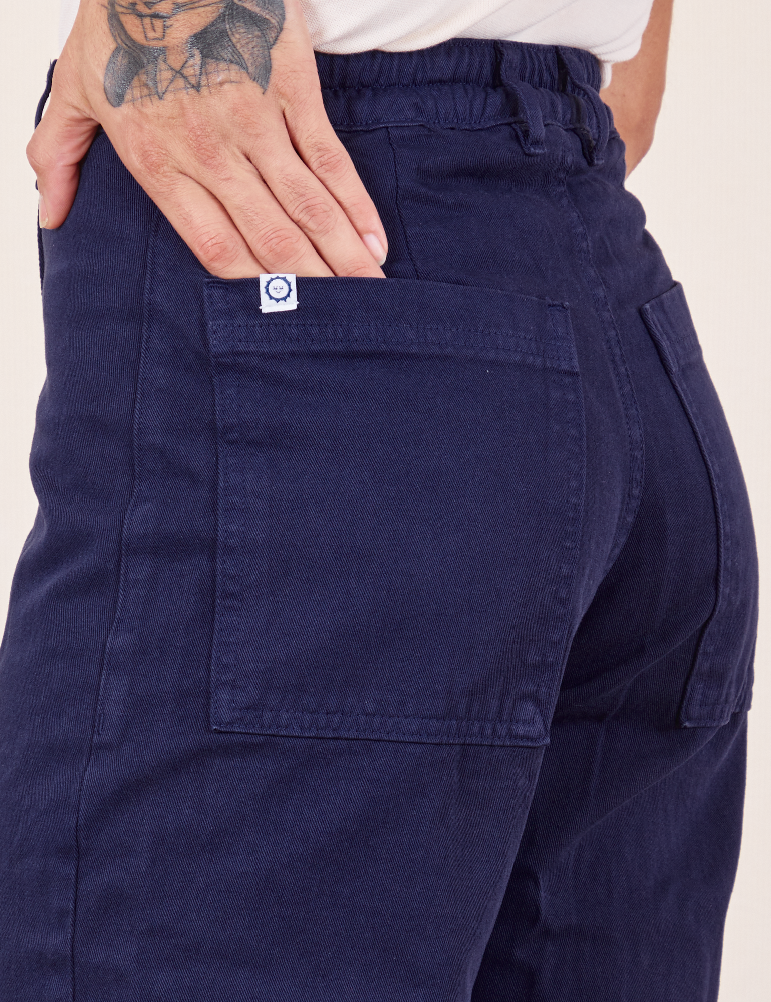Western Pants in Navy back pocket close up. Jesse has their hand tucked into the pocket.