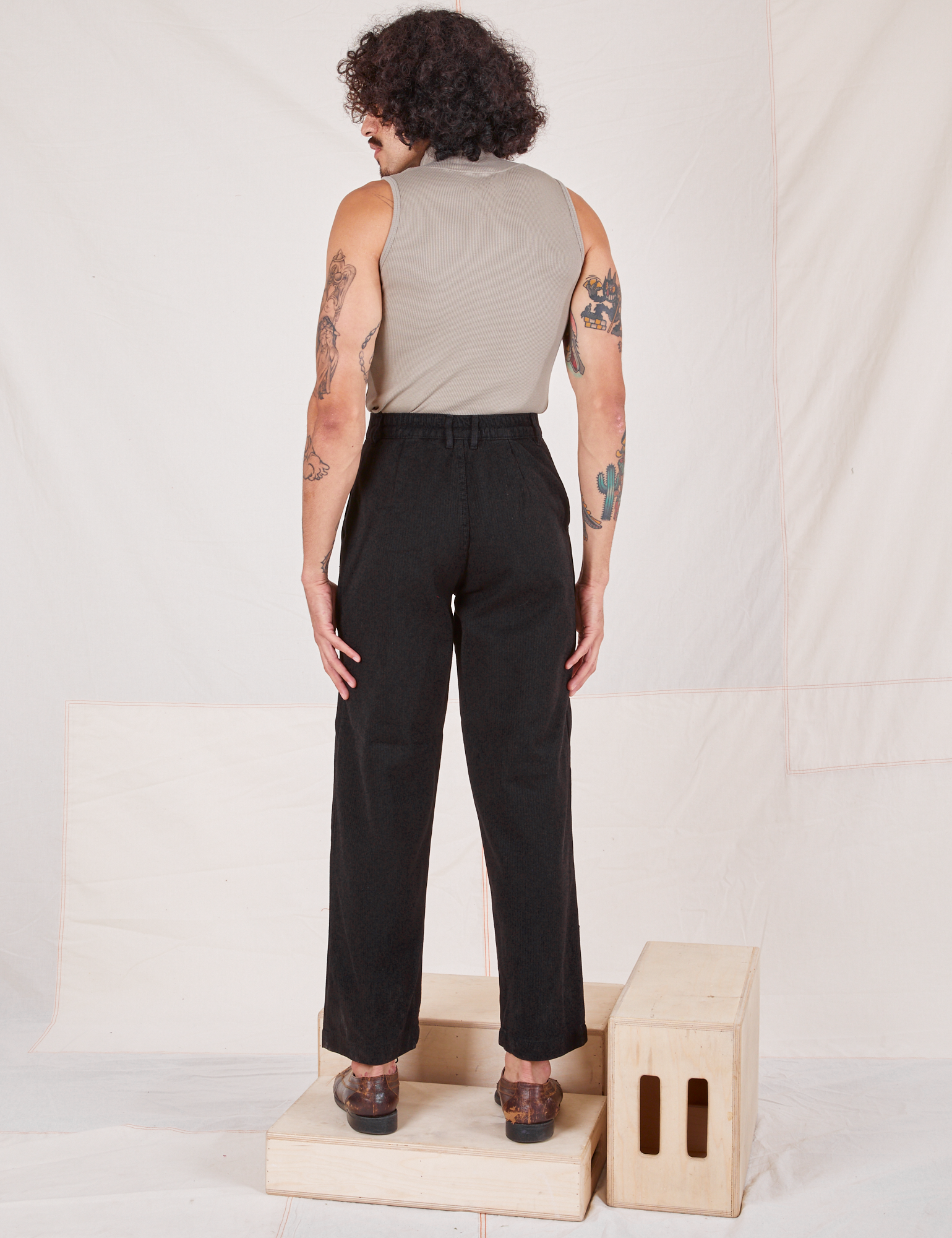 Back view of Heritage Trousers in Basic Black and khaki grey Sleeveless Turtleneck worn by Jesse