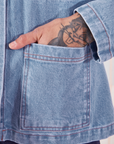 Front pocket close up of Indigo Denim Work Jacket in Light Wash. Jesse has their hand in the pocket.