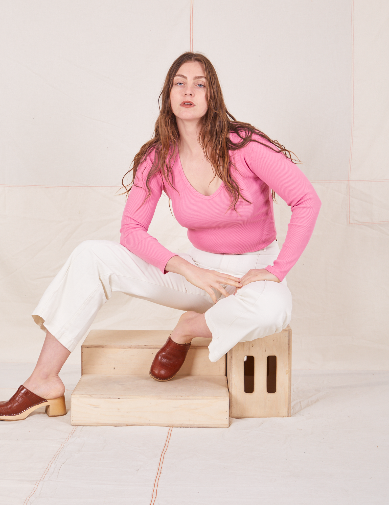 Allison is sitting on a wooden crate wearing Long Sleeve V-Neck Tee in Bubblegum Pink and vintage tee off-white Western Pants