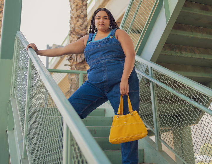 Alicia wearing Overall Handbag in Mustard Yellow, Dark Wash Denim Overalls, and Tank Top in Greek Blue