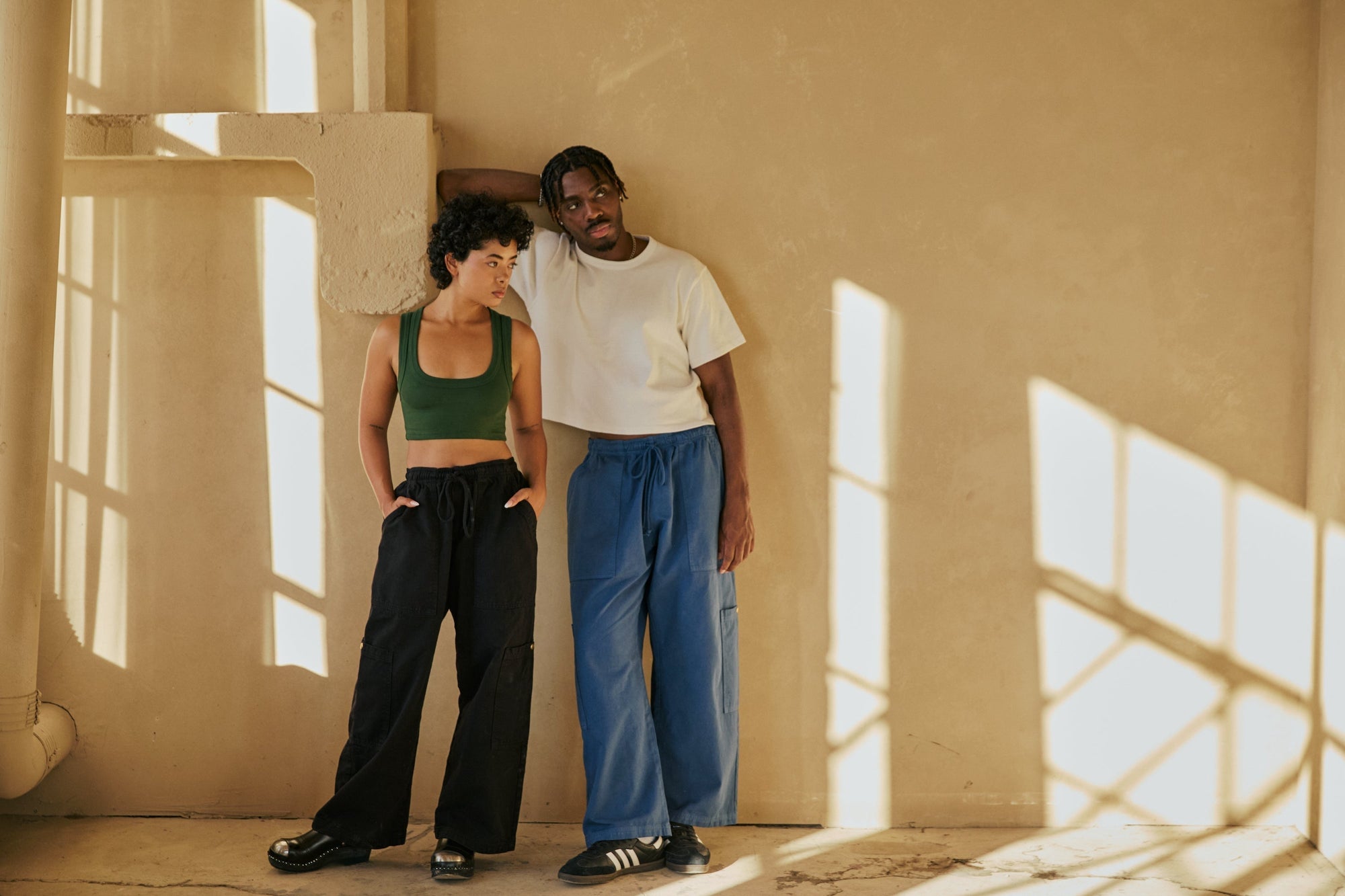 Mika is wearing Drop Pocket Cargo Pant in Basic Black and a Mini Crop Tank in Evergreen. Isaac is wearing Drop Pocket Cargo Pant in French Blue and a Cropped Burly Tee in Vintage Tee White