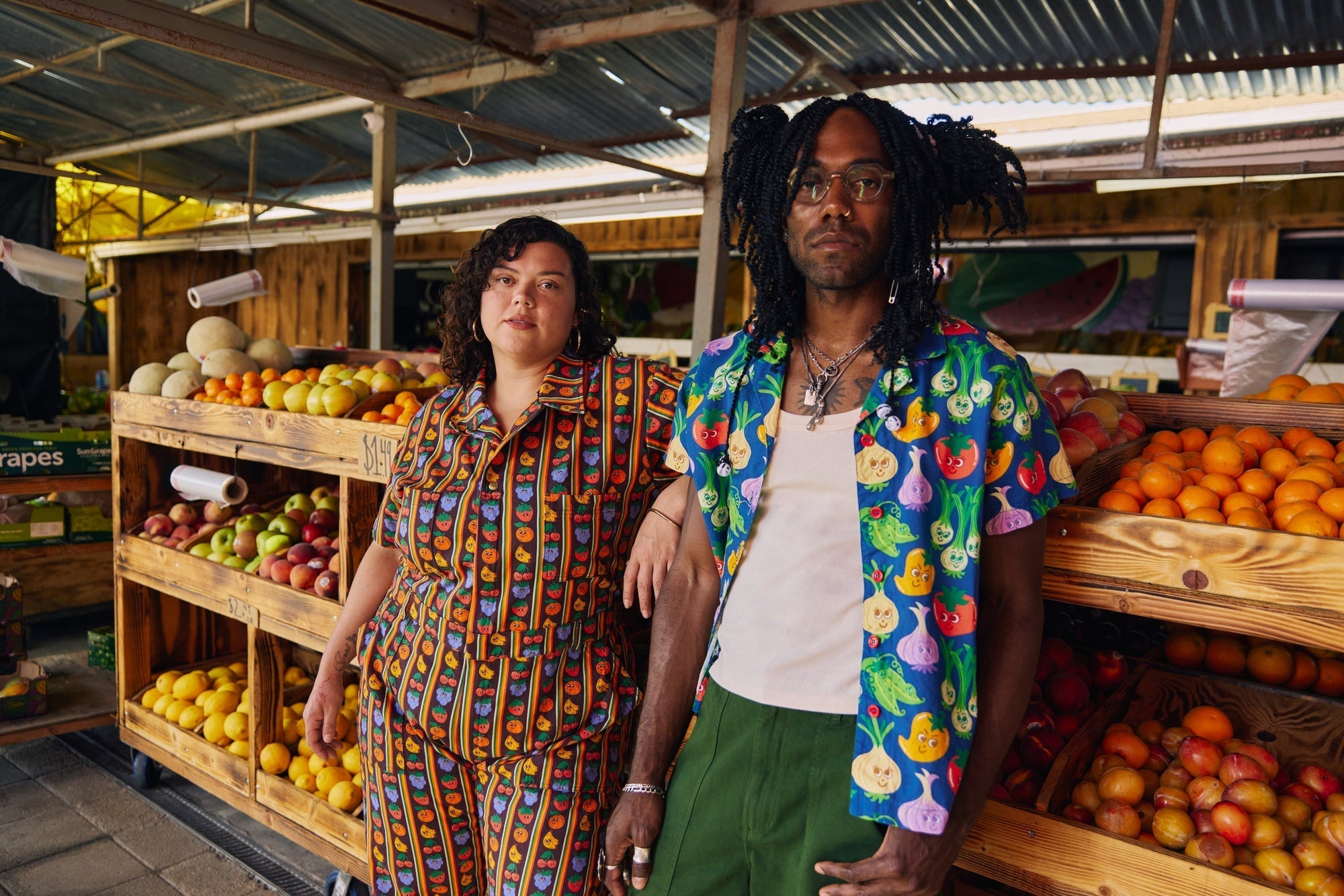 Kristen is wearing the Short Sleeve Jumpsuit in Fruit Fantasy and Jerrod is wearing the Veggie Village Button-Up