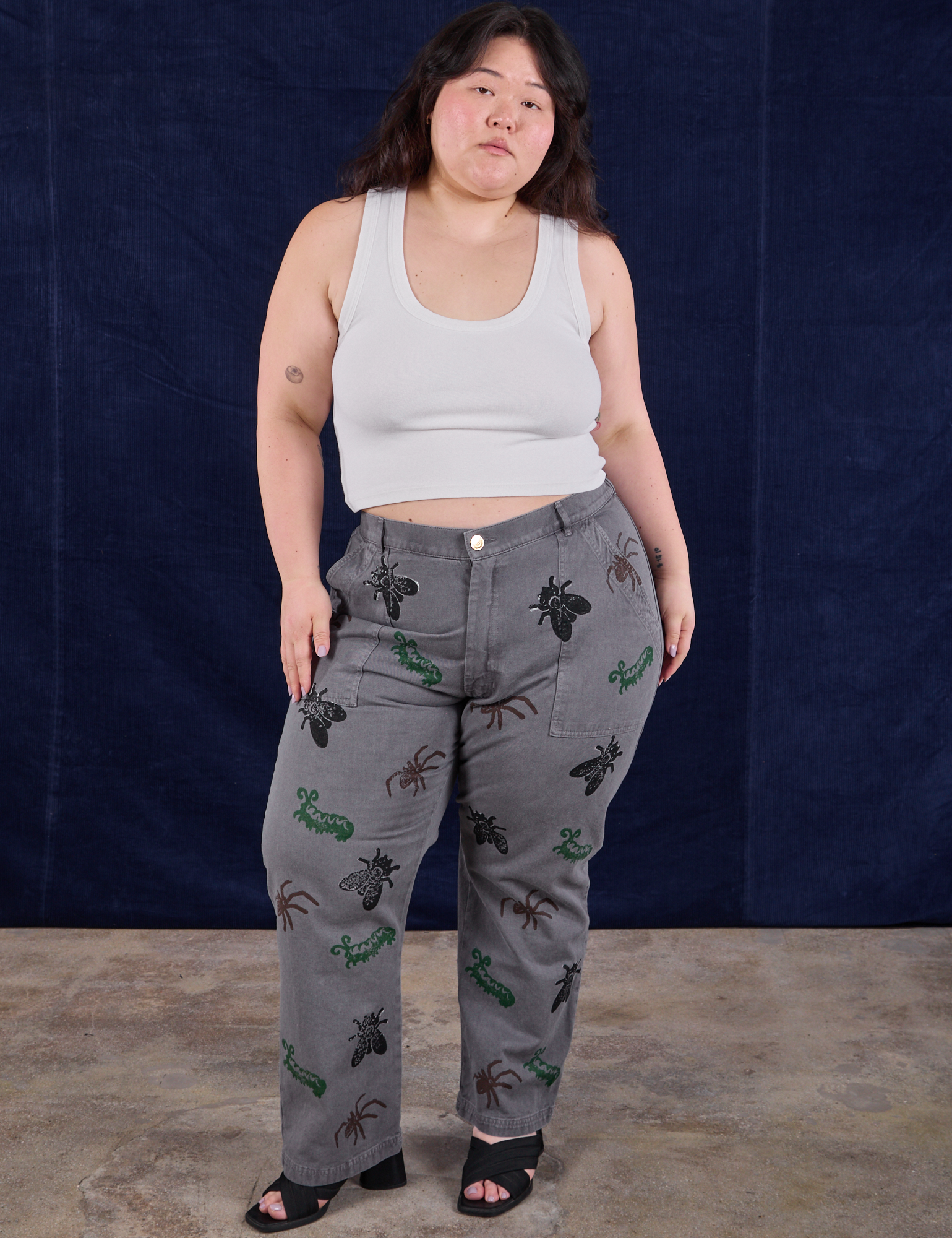 Ashley is 5'7" and wearing 1XL Paintstamped Bug Work Pants in Washed Grey paired with a Cropped Tank in Vintage Tee Off-White