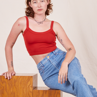 Alex is sitting on a wood block wearing Cropped Cami in Mustang Red and light wash Frontier Jeans