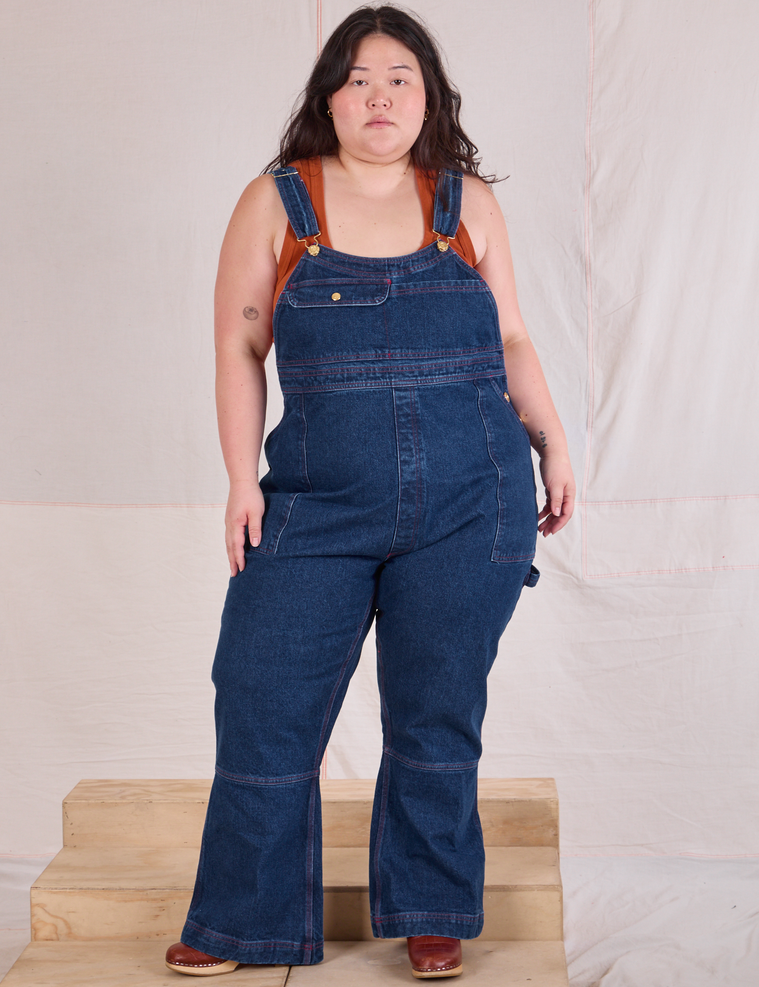 Ashley is 5'7" and wearing 1XL Carpenter Overalls in Dark Wash