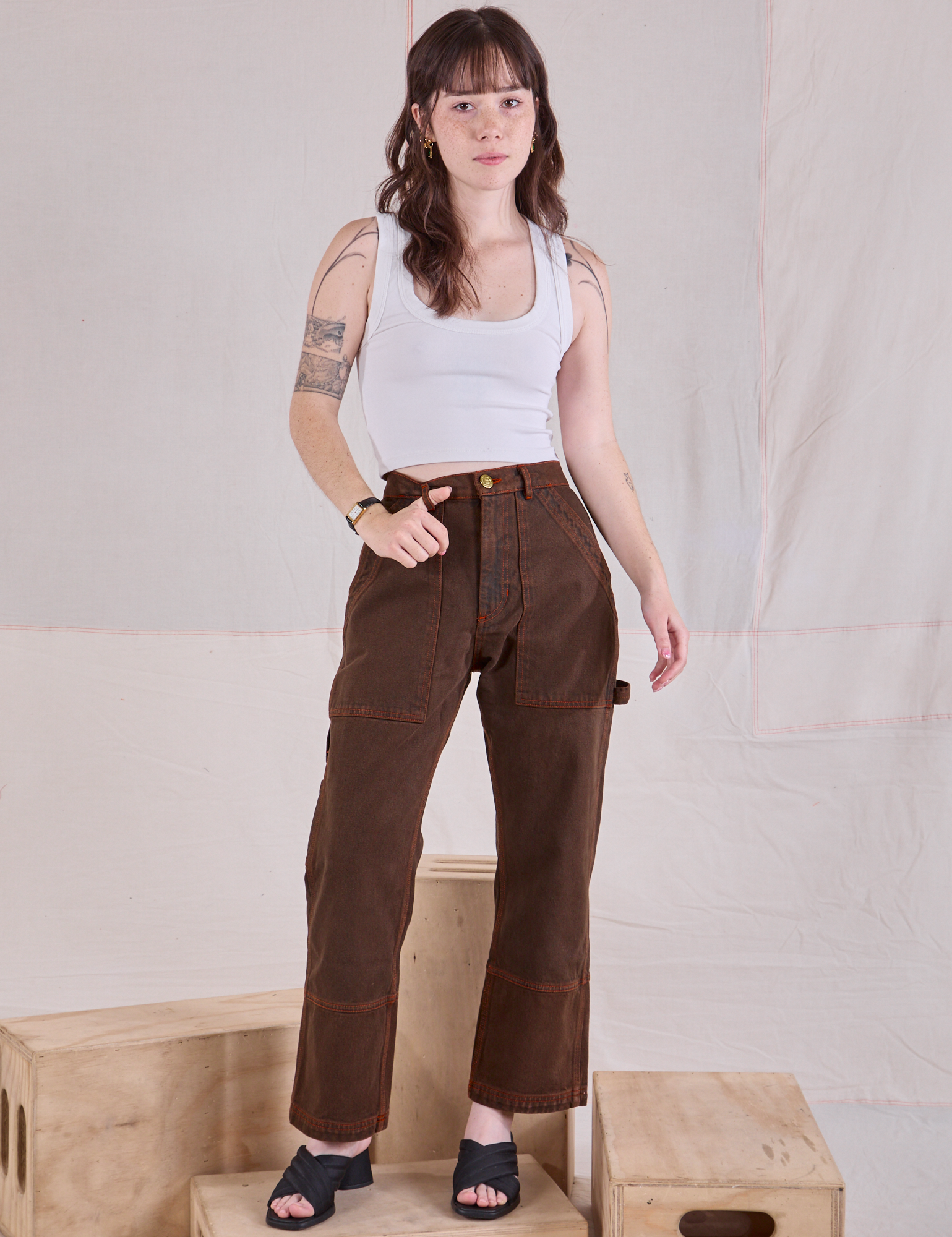 Hana is 5'3" and wearing XXS Petite Overdyed Carpenter Jeans in Fudge paired with a Cropped Tank in vintage tee off-white