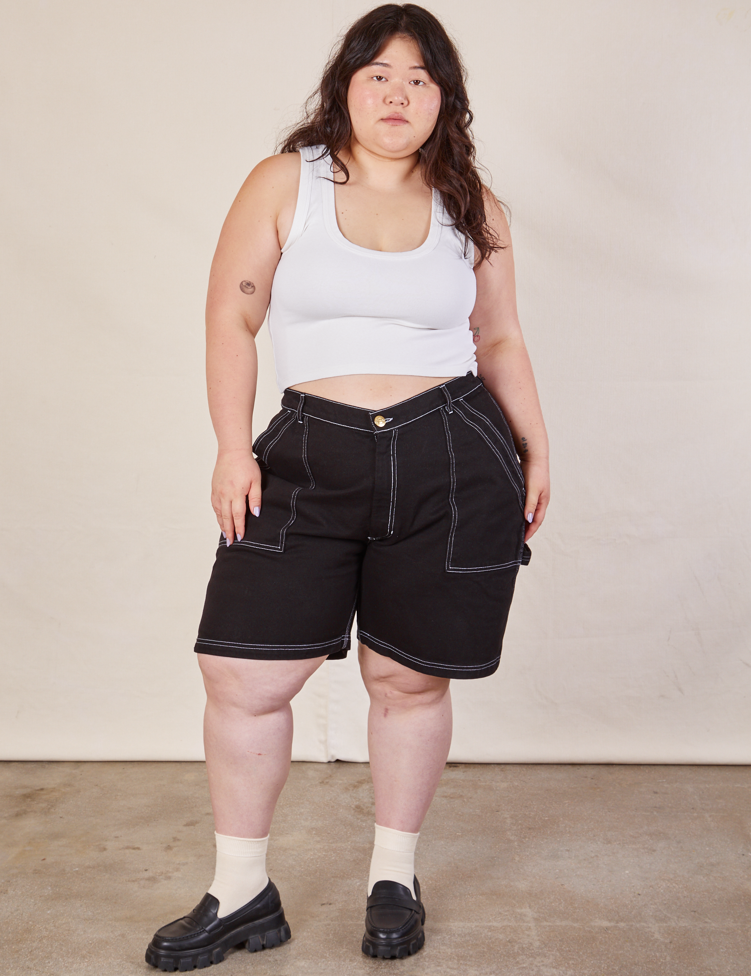 Ashley is 5'7" and wearing 1XL Carpenter Shorts in Basic Black paired with a Cropped Tank in vintage tee off-white