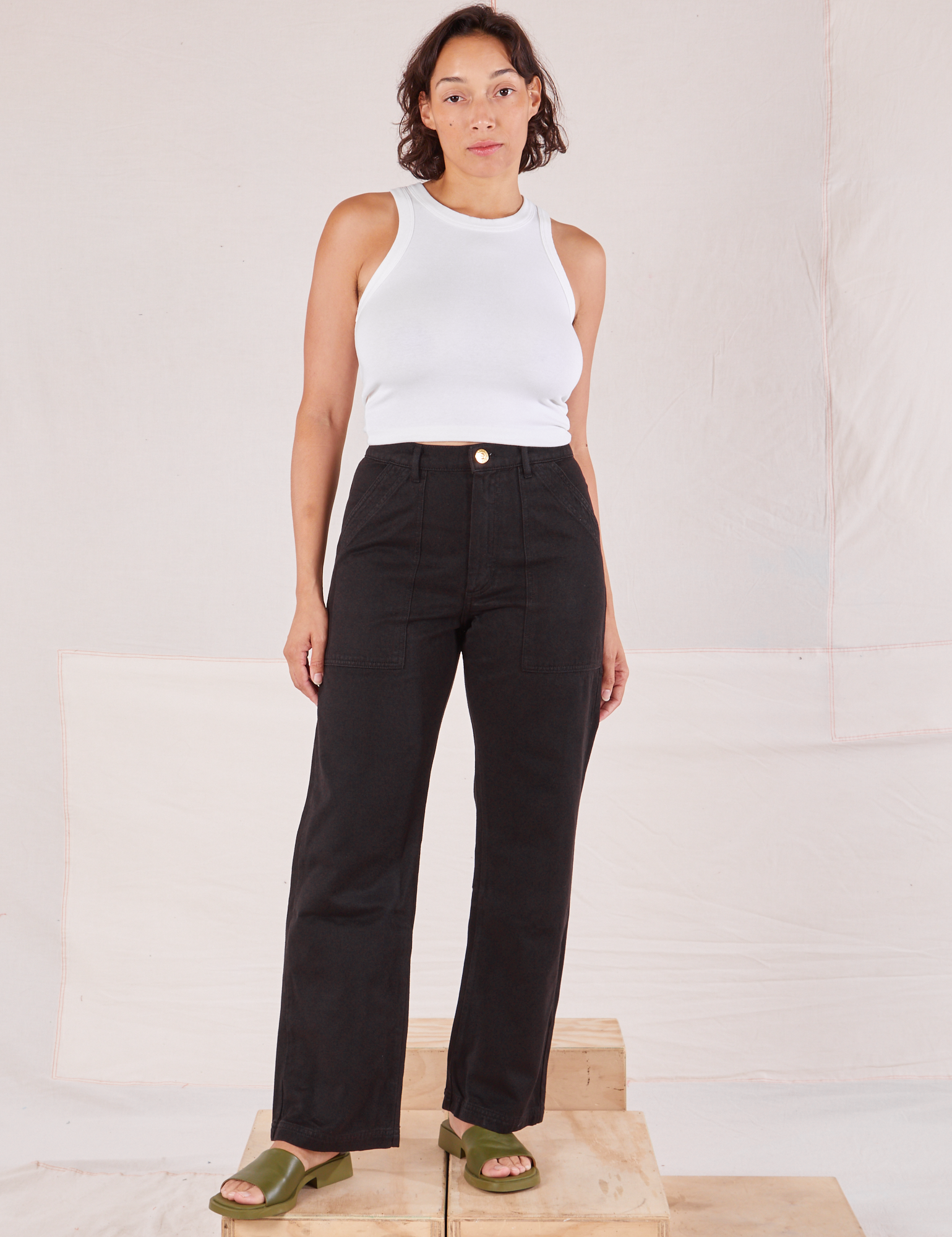 Tiara is 5'4" and wearing S Organic Work Pants in Basic Black paired with a Racerback Tank in vintage tee off-white