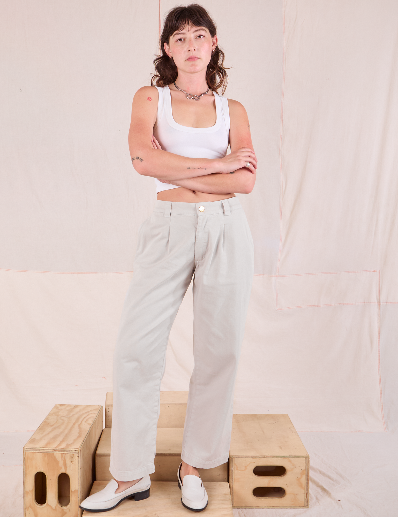 Alex is 5&#39;8&quot; and wearing XXS Mid-Rise Pleated Trousers in Stone White paired with a Cropped Tank in vintage tee off-white