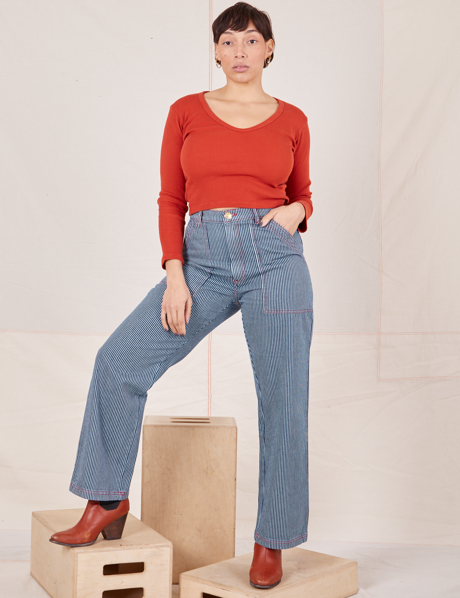 Tiara is 5'4" and wearing S Railroad Stripe Denim Work Pants paired with a paprika Long Sleeve V-Neck Tee