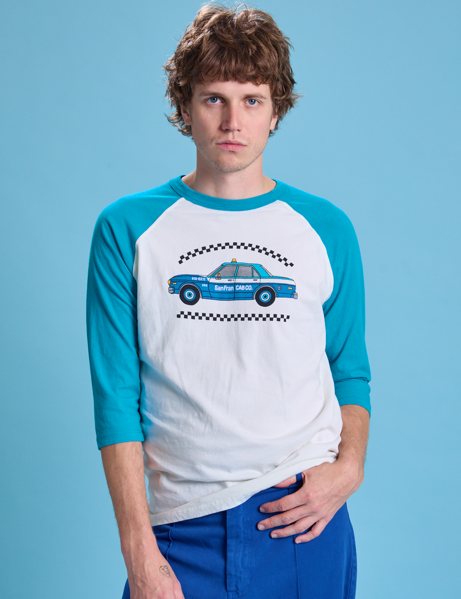 Quinn is 6'3" and wearing M Taxi Raglan Tee in San Francisco. White tee body with blue raglan sleeves.