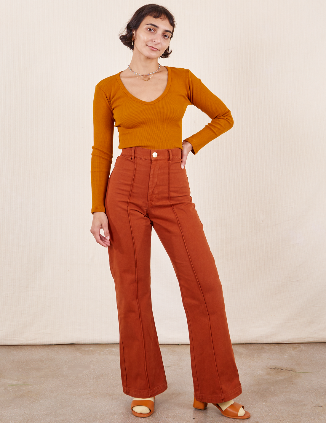 Soraya is 5'2" and wearing XXS Petite Western Pants in Burnt Terracotta paired with a burnt orange Long Sleeve V-Neck Tee. 