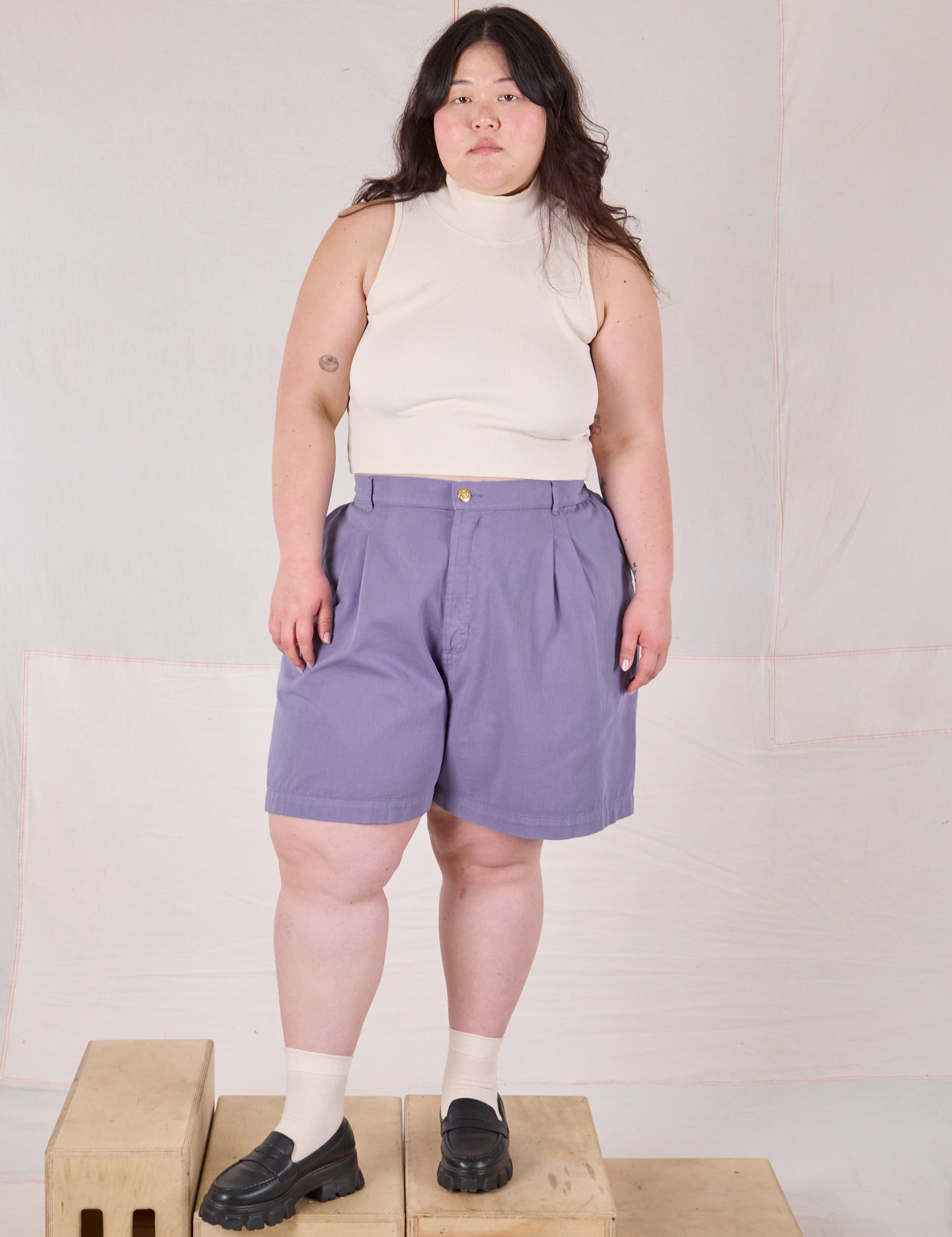Ashley is 5’7” and wearing 1XL Trouser Shorts in Faded Grape paired with a Sleeveless Turtleneck in Vintage Tee Off-White