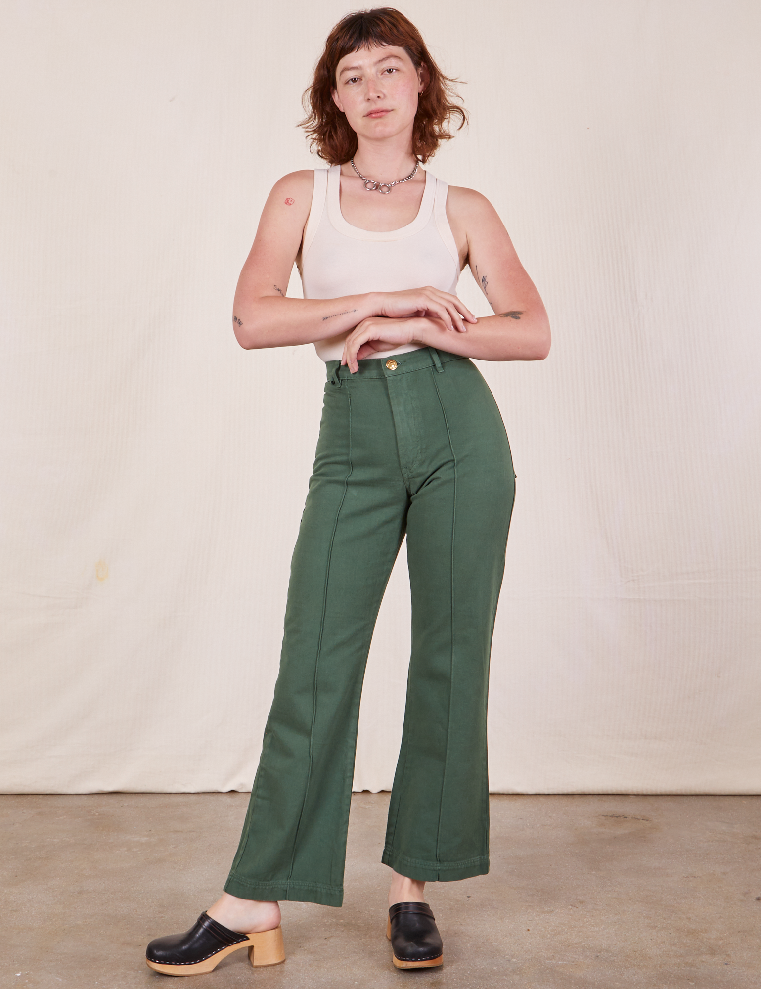 Alex is 5&#39;8&quot; and wearing XS Western Pants in Dark Green Emerald paired with a vintage off-white Tank Top