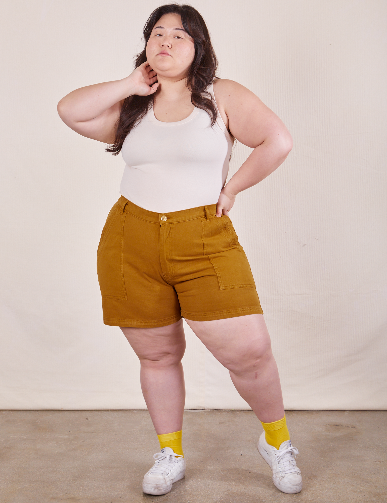 Ashley is 5’7” and wearing 1XL Classic Work Shorts in Spicy Mustard paired with a Tank Top in vintage tee off-white