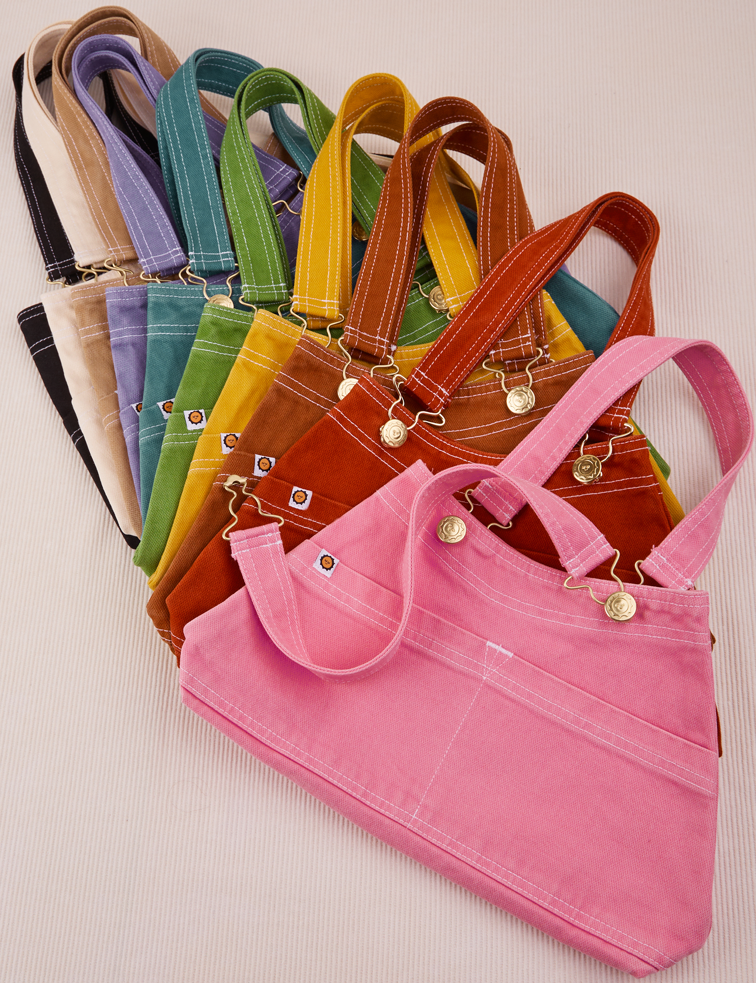 Overall Handbags in a rainbow of colors. Stacked one each other and fanned out.