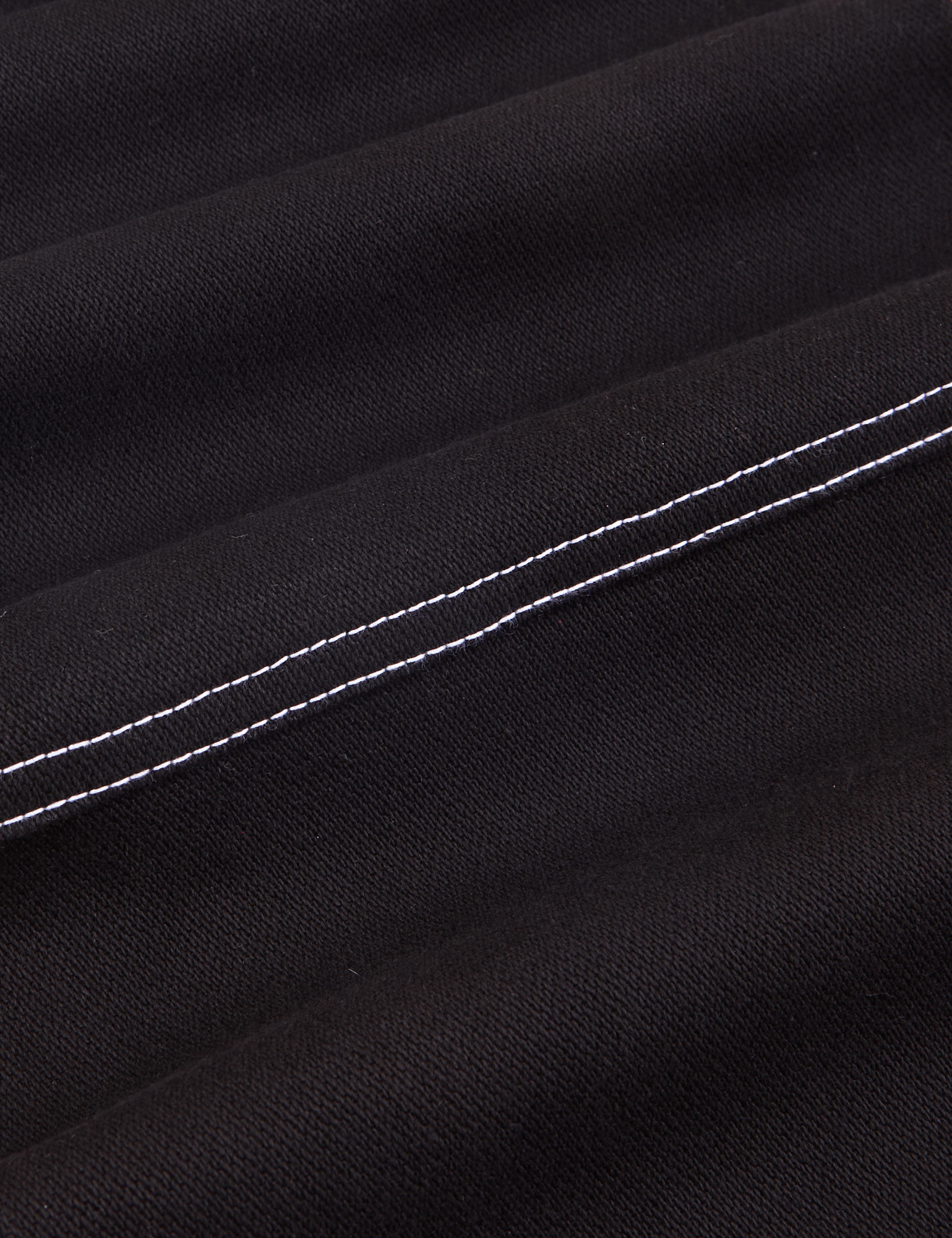 Carpenter Jeans in Black fabric detail close up. White stitching on pants.